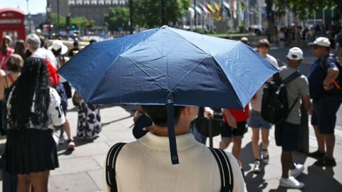 A tourist in Parliament Square, London, holds a blue umbrella to protect themselves from the hot weather on 11 August 2025.
