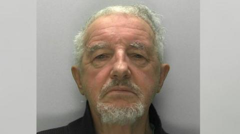 A custody image of Philip Wood. He has coarse, curly white hair cut short, a white goatee and thick grey eyebrows. 