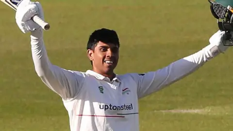 Rishi Patel with both arms aloft after scoring a century