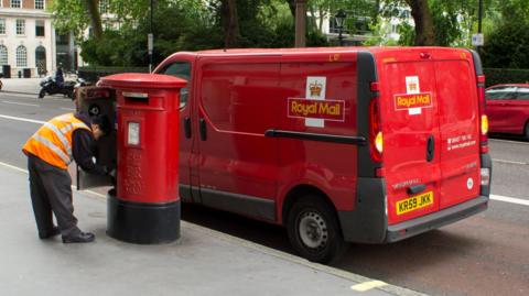 A Royal Mail post van next to a post box where a postal worker is emptying letters