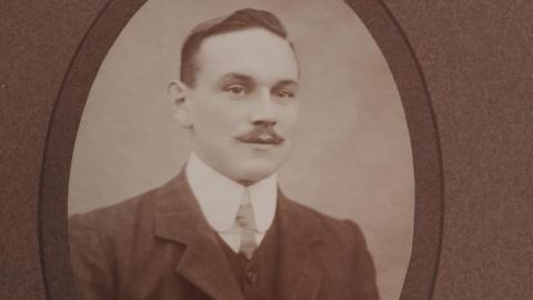 Sgt John Smith in a black and white photo. He is wearing a suit, waistcoat and tie