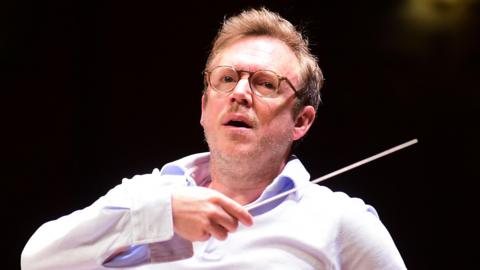 Daniel Harding in an open-necked white shirt with an arm raised holding a conductor's baton conducting the Orchestra Santa Cecilia of Roma in Bologna on 8 May 2026