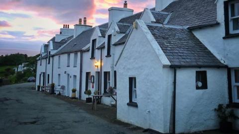 The restaurant is a white walled building. It is pictured at dusk with a pink sky behind it.