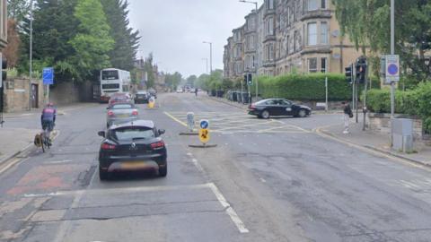 Dalkeith Road has a line of cars and a bus travelling along it at a crossroads.
