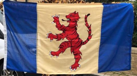 A flag featuring a red heraldic tiger facing to the left. It sits on a yellow stripe with a dark blue stripe on either side. 