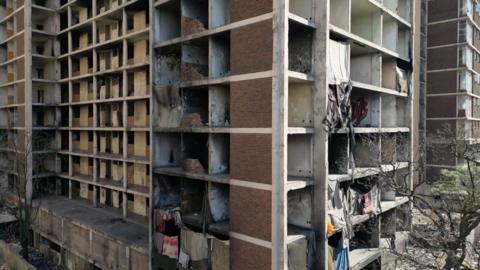 A drone shot of the side of an abandoned building. The facade is covered in cloths providing protection for some of those living inside.