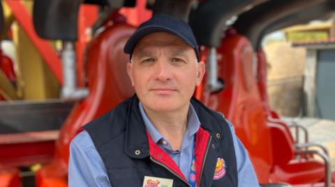 A man in a blue baseball cap sits on the seat of a thrill ride at Crealy Theme Park and Resort in Devon