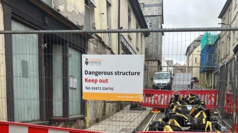 A photo which shows metal fencing put up where the road closure in Camelford was, with a sign from Cornwall Council on it saying "dangerous structure, keep out"