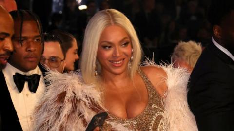 Beyonce at the grammy awards, smiling. wearing a gold dress, with blond hair.