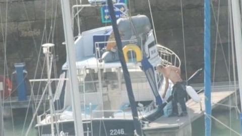 a shirtless man approaches a blue and white boat