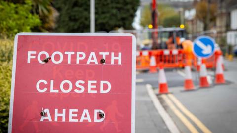 Generic image of roadworks in the UK with a sign that reads Footpath Closed Ahead