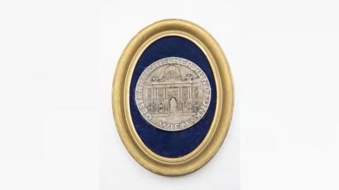 Pale gold medal with image of classical domed building on the front