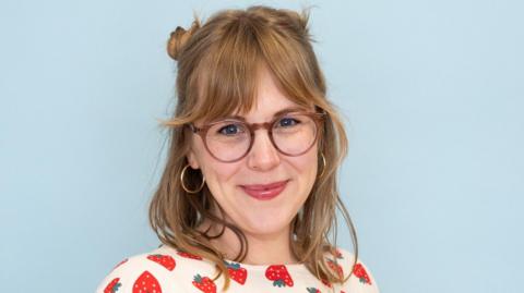 Jenny Lennick smiles at the camera. She is wearing glasses and a top with a strawberry pattern