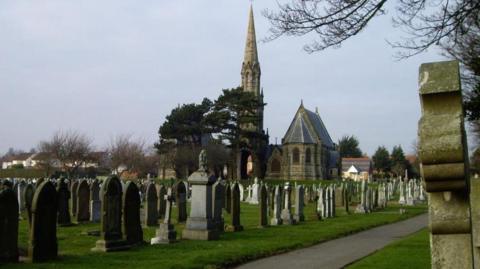 Rows of tombstones in a graveyard with a church building in the background.