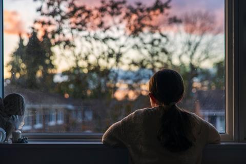 a child staring out the window looking across a street as the sun is setting