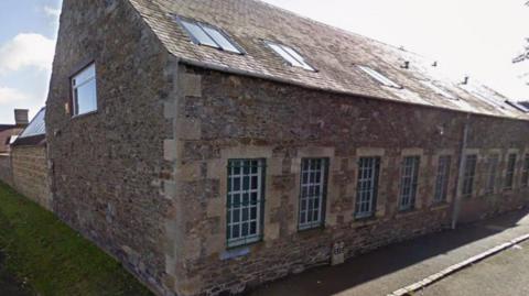 A mill building in the Borders - it is a low, brick building with a lot of barred windows on it