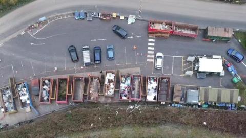 A drone shot of the Lower Compton recycling centre. A row of large metal skips can be seen from above, with parking spaces next to them and several cars parked up. There is a road next to it.