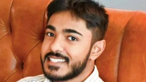 Anugrah Abraham, a man with black hair and facial hair, smiles into the camera. He is sat on brown leather sofa and the top of his shirt, which appears to be pinstriped, is visible.