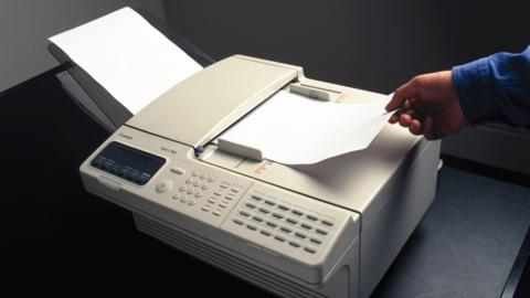 A man removes a piece of paper from a fax machine
