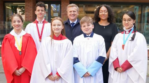 Five choristers and a man and a woman posing for a picture