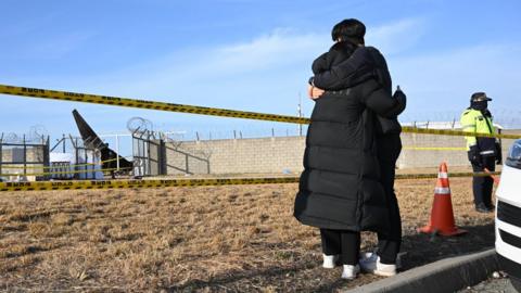 Two mourners embrace each other near the scene where a Jeju Air Boeing 737-800 series aircraft crashed at Muan International Airport