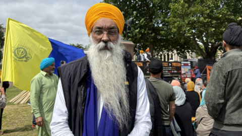 A Sikh man wearing an orange turban at a march in London. He is looking into the camera.