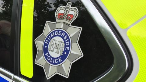 The Humberside Police logo with Humberside Police in a blue circle, ER in the middle and a star and crown around it. Located on the side of a police car