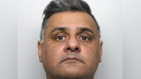 A custody image of a man with short, dark grey hair with a neutral expression.  