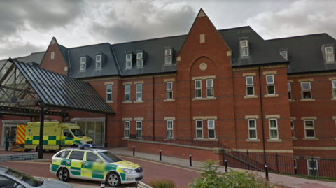 Front of hospital building with green and yellow ambulance and green and yellow doctor's car outside.