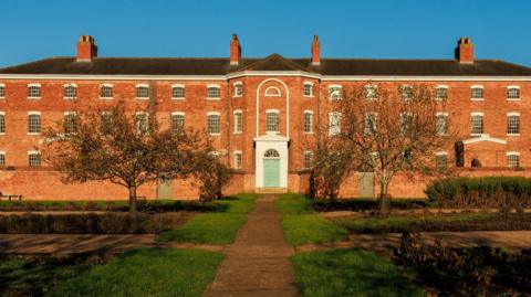 Frontage of Southwell Workhouse, a three storey brick heritage building set in a  large garden area