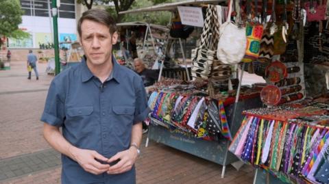 BBC correspondent Will Grant standing in front of market stall