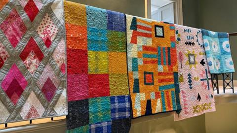 A range of colourful quilts hanging off a railing