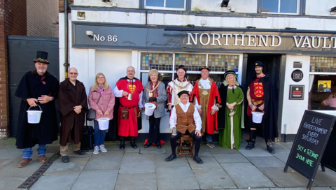 Image shows 10 people standing in front of a pub, with some dressed in medieval dress 