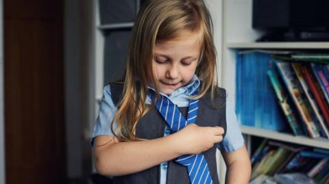 A young girl tying her school tie