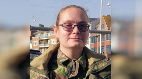 A woman with glasses and a camo jacket.