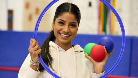 Presenter Shini Muthukrishnan  holding a blue hoop and three coloured balls - for boccia.