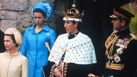 Prince Charles, wearing the crown after being invested with the title Prince of Wales, on a balcony with The Queen and Prince Philip