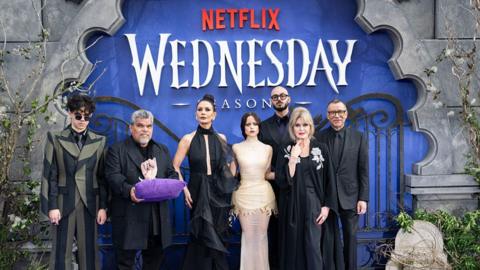 Cast of Wednesday at the season two London premiere, standing in front of a sign