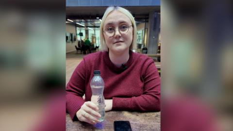 Georgina Hayes sits at a table holding a bottle of water