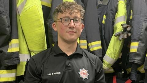 Anthony Seaward sitting in front of firefighter uniforms