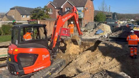 A small orange and black digger digging up a road in a residential street.