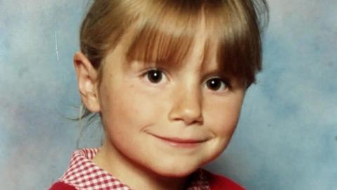 An eight-year-old girl with blonde hair, dark brown eyes and wearing a red jumper. 