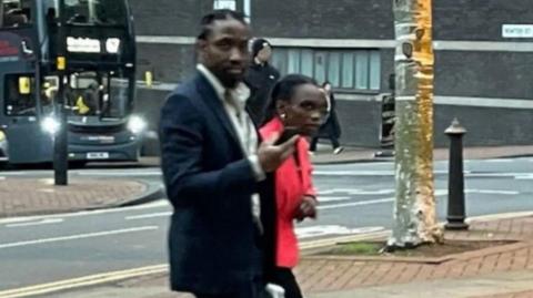 Tai Yasharahyalah, in a black suit, and Naiyahmi Yasharahyalah, in a red jacket, walking to court
