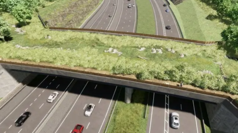 Cars travel along a busy road and travel under a bridge covered in grass.