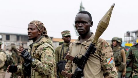 Members of the M23 rebel group gather, armed with weapons and wearing military fatigues