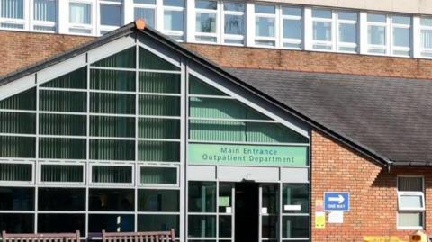 The main entrance of Shotley Bridge Hospital. It is a brown brick building with two brown wooden benches in front of it.