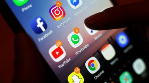 A thumb over a smartphone screen that is several social media app icons on it.