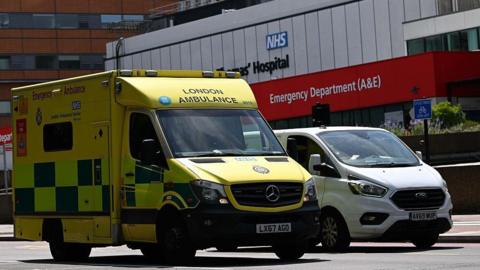 Yellow London Ambulance Service ambulance parked outside an NHS hospital emergency department (A&E).