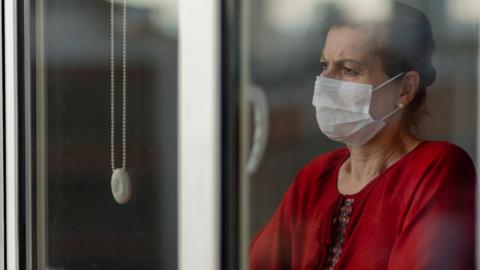 Concerned Asian woman wearing a face mask looking out of the window