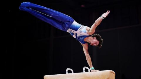 Reuben Ward of Team Scotland competes in Pommel Horse. He is wearing bright blue and has curly brown hair.